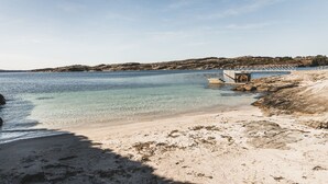 Een strand met helder water, een rotsachtige kustlijn en een klein pier.