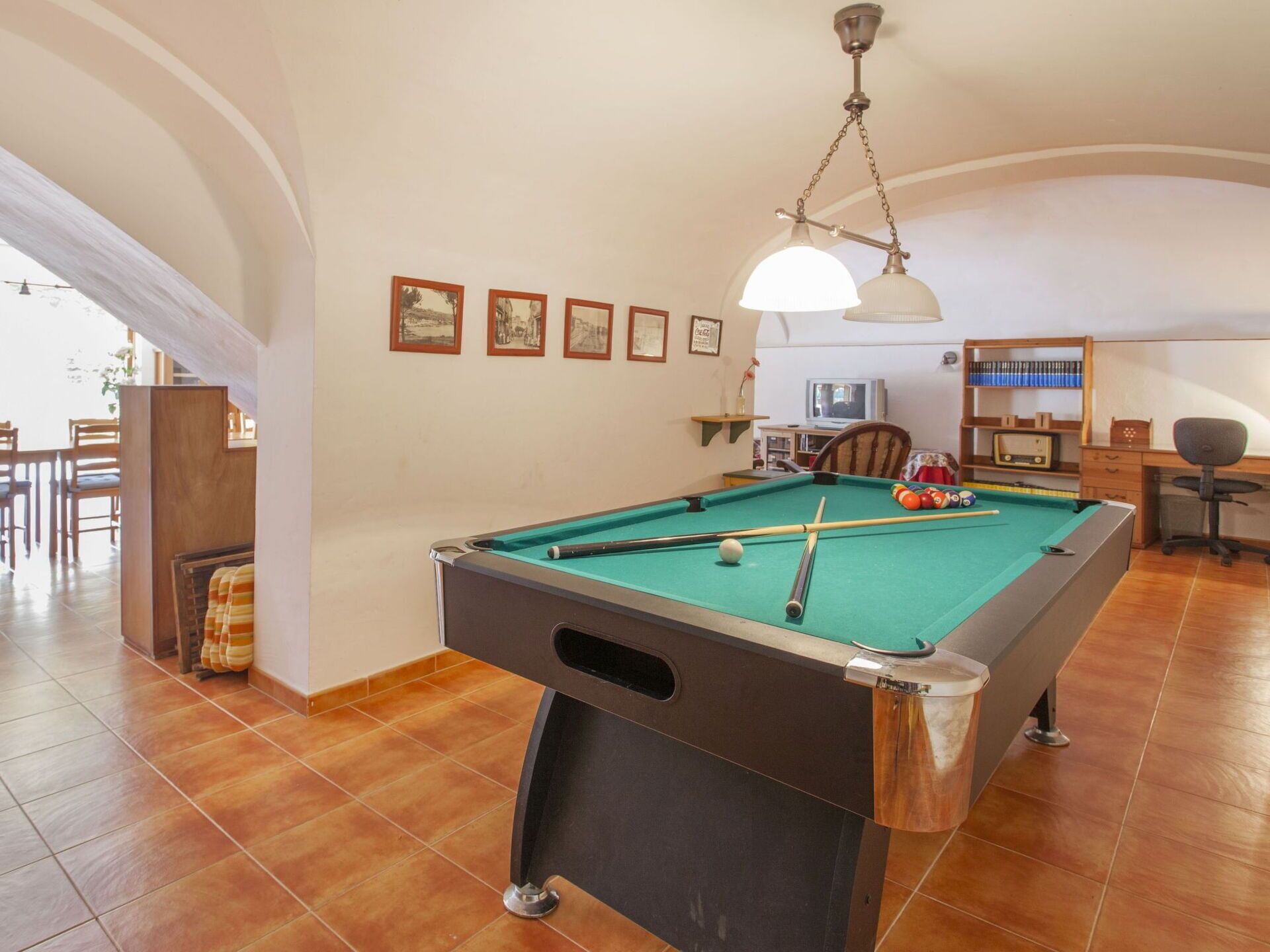 A pool table in a room with a dining area, a television, and a bookshelf.