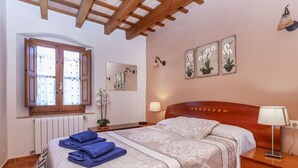 A bedroom with a wooden headboard, a large window with curtains, a bedside lamp, and a bed with a patterned bedspread and folded towels. - Beautiful private villa for 8 guests with WIFI, private pool, TV, patio and pets allowed (Calonge)