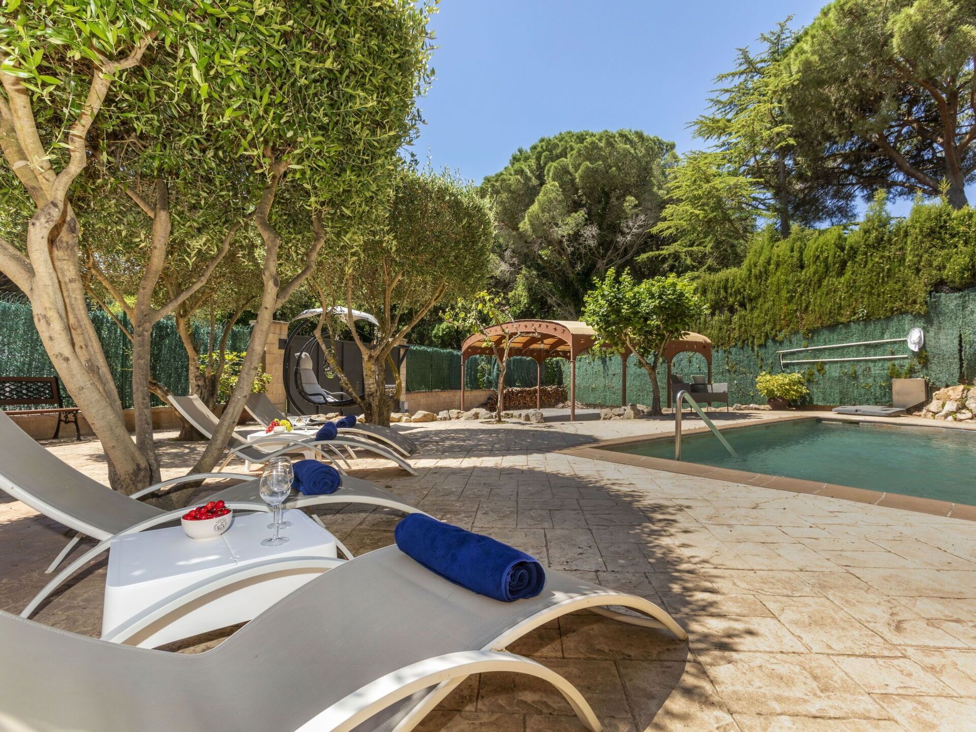 Un espace aménagé au bord de la piscine, avec des chaises longues, une table avec un verre et une pergola.