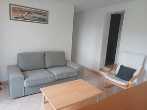 Un salon avec un canapé gris, une table basse en bois et un fauteuil blanc.