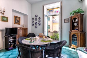 Un comedor con una mesa redonda, sillas de mimbre, un televisor y un mueble con objetos decorativos.