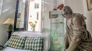 A room with a bed, a green checkered pillow, a glass cabinet with decorative items, and a statue. - Dora Flat   Amalfi centre (doorbell)