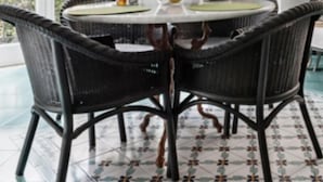 A dining area with a round table, wicker chairs, a cabinet with tea sets, and a potted plant. - Dora Flat   Amalfi centre (doorbell)
