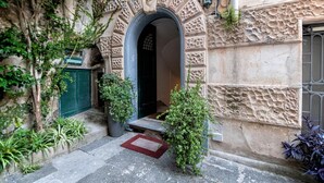 A stone building with an ornate entrance, a green door, and potted plants. - Dora Flat   Amalfi centre (doorbell)