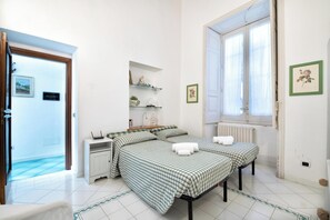 Un dormitorio con dos camas, una mesita de noche pequeña, un radiador y una ventana con cortinas.