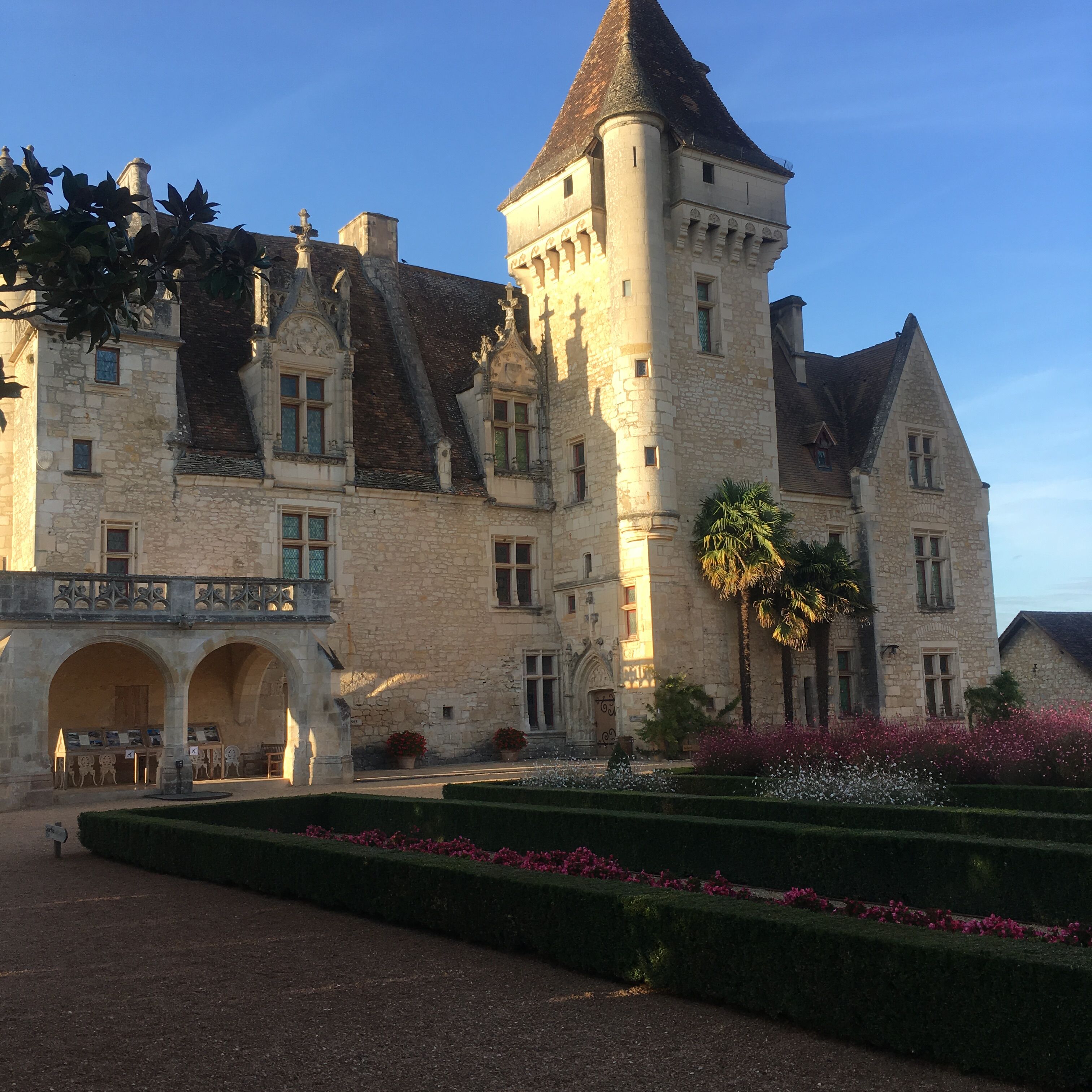 A historic stone building with a central tower, arched entrance, and a formal garden.