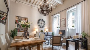 A cozy living room with a wooden dining table, comfortable seating, a large clock, and a chandelier. - Modern comfort in Lucca's Picturesque Canal District (Lucca)