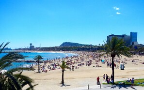 A crowded beach with palm trees and a clear blue sky. - Stylish Barcelona Apartment | Prime Location near Las Ramblas! (Barcelona)
