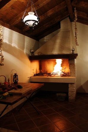 Una cocina rústica con estufa de leña, lámpara colgante y piso de baldosas.