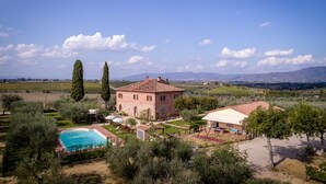Una villa con piscina, rodeada de olivos y viñedos, con vistas a montañas distantes.