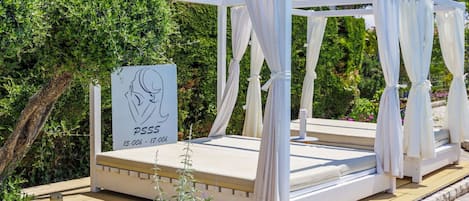 A white outdoor bed with a canopy, a sign with a woman's silhouette, and a time schedule.