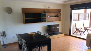 Een woonkamer met een eettafel, stoelen, een televisie en een schuifdeur naar een buitenruimte met stoelen.