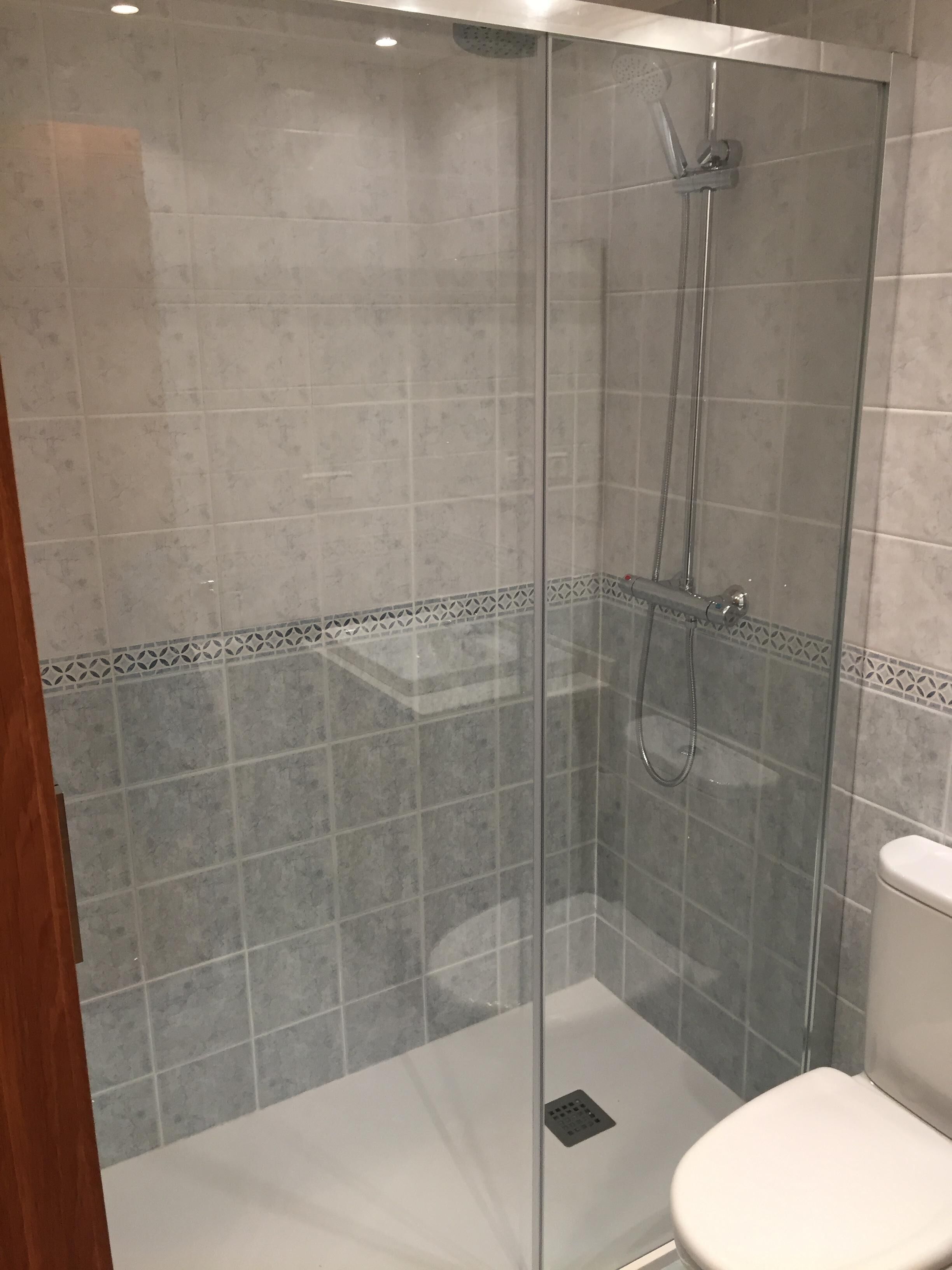 A glass-enclosed shower stall with a tiled floor and a toilet to the right.