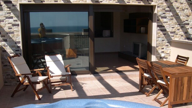 Een zwembadgedeelte met een jacuzzi, houten ligbedden en een eettafel met stoelen.