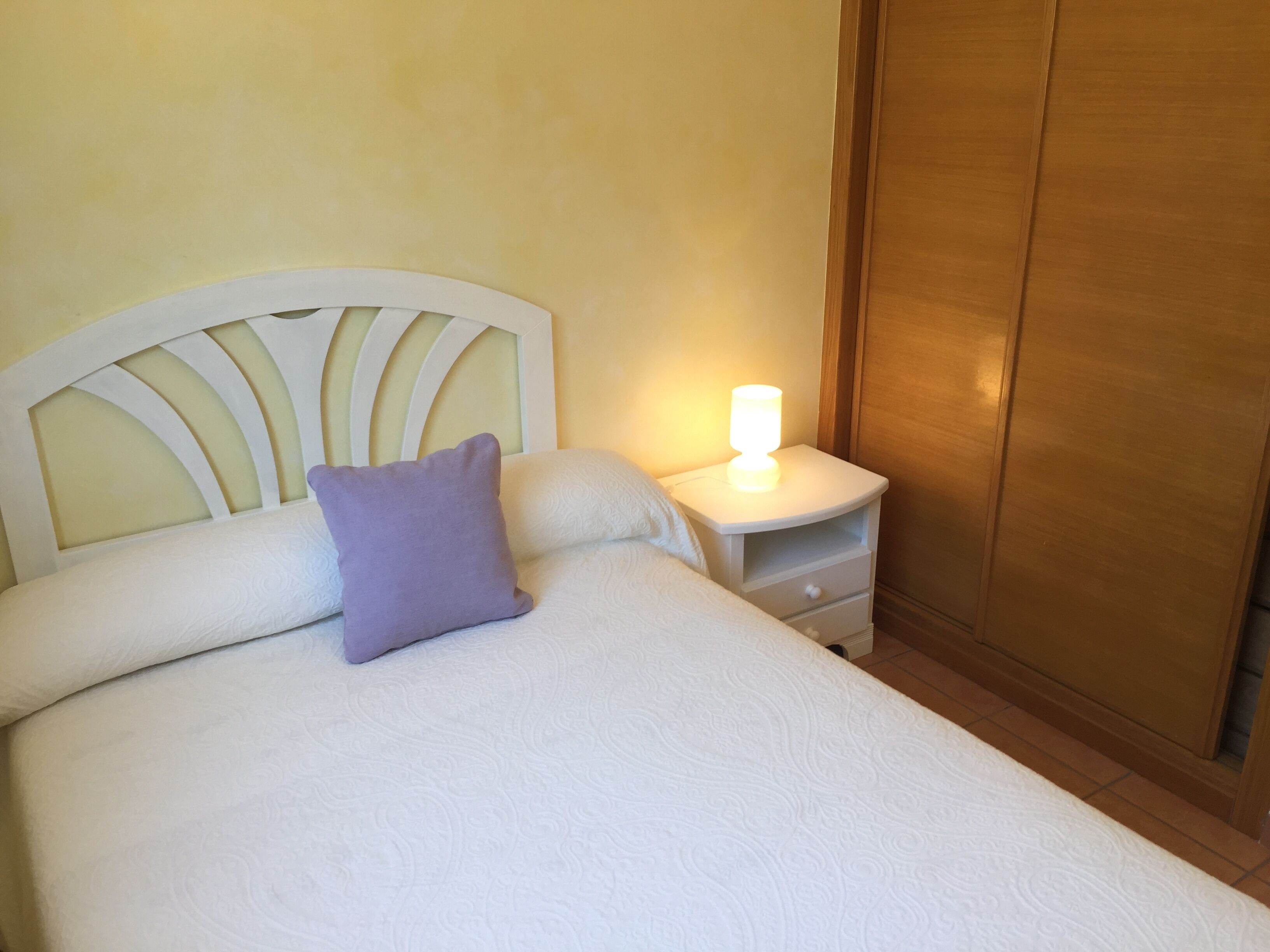 Un lit bien fait, avec une tête de lit, une table de chevet avec une lampe et une armoire en bois.