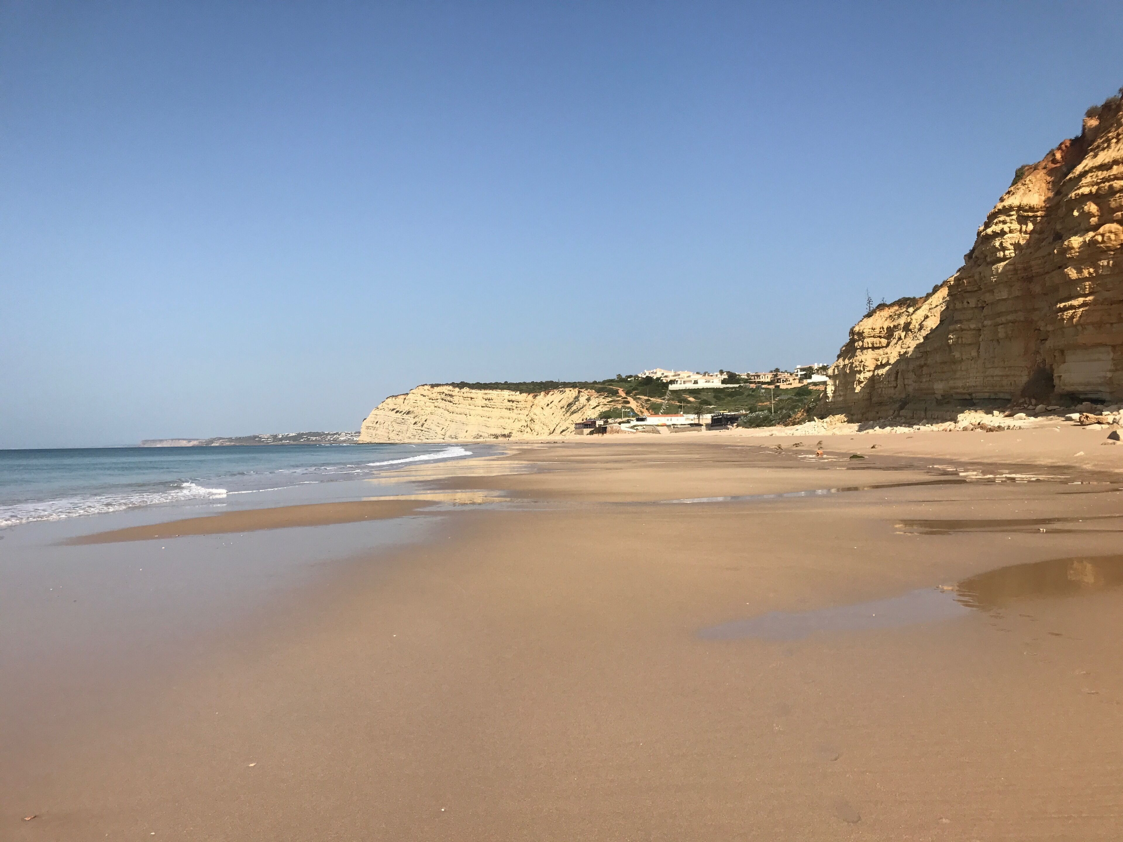 A sandy beach with a rocky cliff and a clear sky.