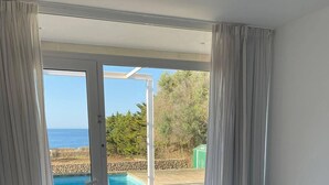 Een slaapkamer met twee bedden, een glazen schuifdeur naar een zwembad en uitzicht op zee.