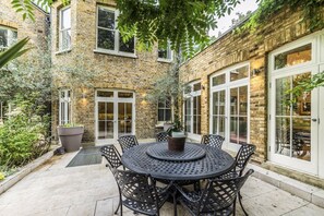 Relax in the serene courtyard, surrounded by a brick wall and large windows, with a round table and matching chairs.