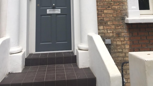 A front view of a house with a grey door, white columns, and a brick wall. - Stylish Luxury Apartment in Earls Court /Chelsea London (London)