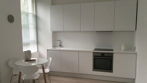 A modern kitchen with white cabinets, a built-in oven, and a dining area with a white table and chairs. - Stylish Luxury Apartment in Earls Court /Chelsea London (London)