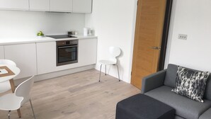 A modern kitchen with white cabinets, a built-in oven, and a dining area with a white table and chairs. - Stylish Luxury Apartment in Earls Court /Chelsea London (London)
