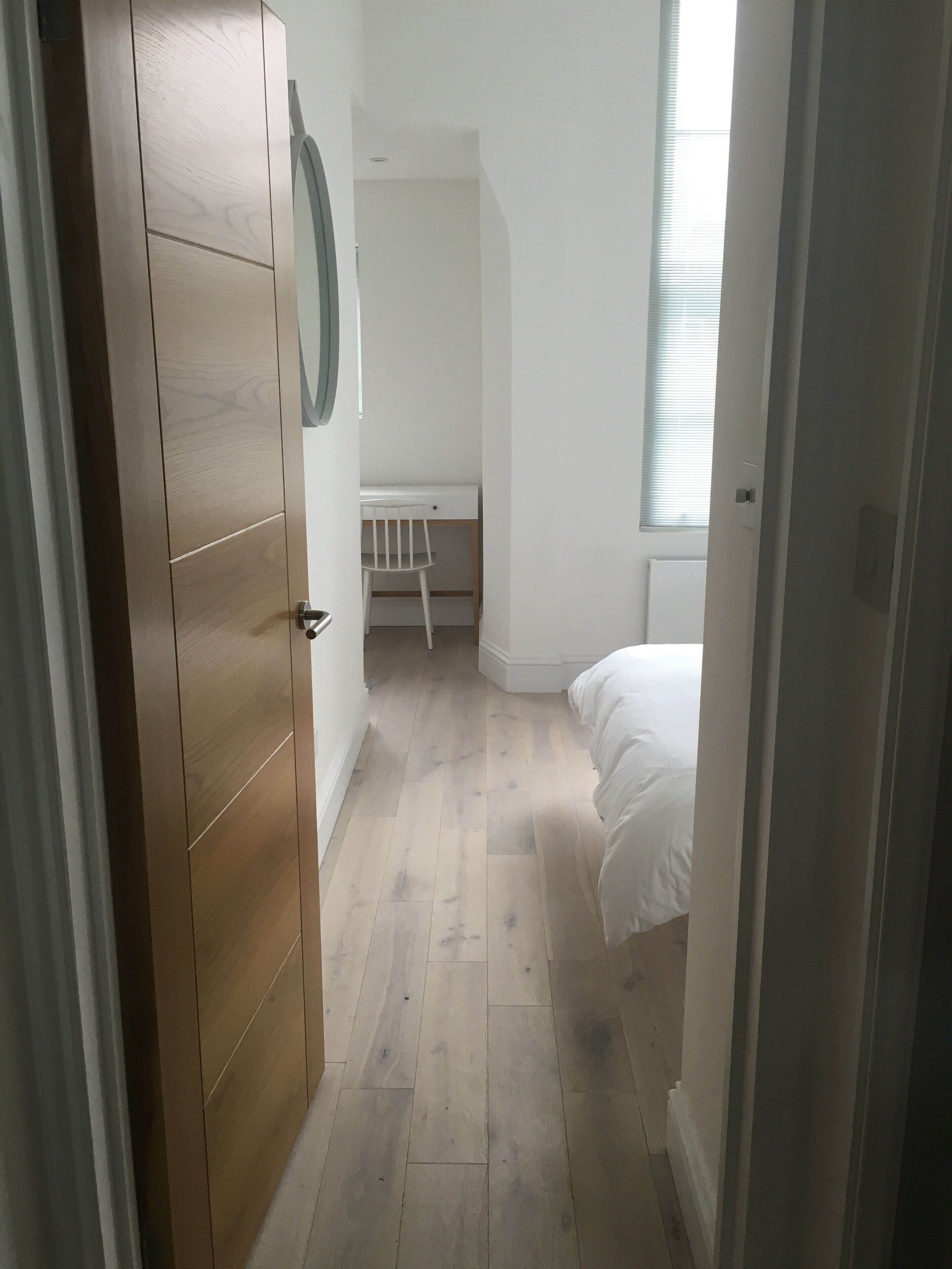 A narrow hallway leading to a bedroom with a bed, a desk, and a chair.