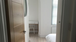 A narrow hallway leading to a bedroom with a bed, a desk, and a chair. - Stylish Luxury Apartment in Earls Court /Chelsea London (London)
