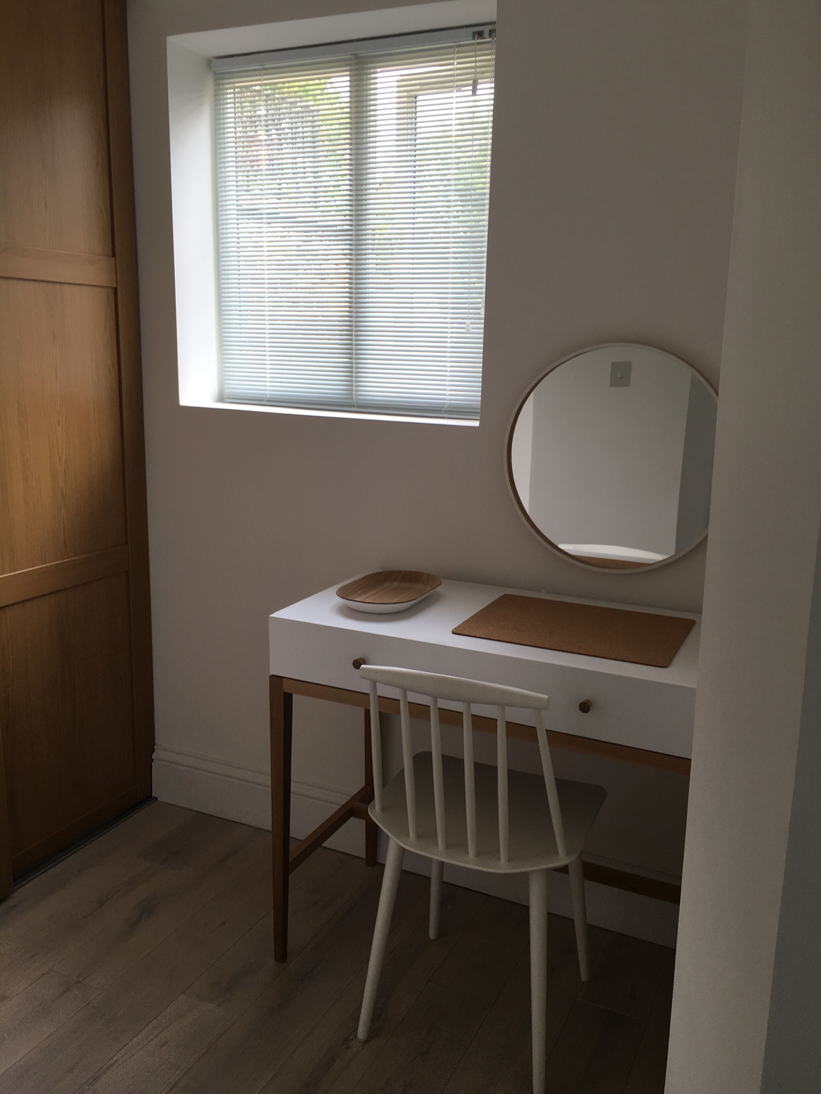 A small, well-lit room with a desk, chair, and a window with blinds.