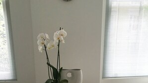 A small dining area with a round table, two white chairs, a potted plant, a wooden tray, and a clock on the wall. - Stylish Luxury Apartment in Earls Court /Chelsea London (London)