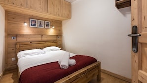 A wooden bed with a red blanket and white linens, a wooden headboard, and a small shelf above the bed. - Marcel -  an apartment that sleeps 4 guests  in 1 bedroom (Chamonix)