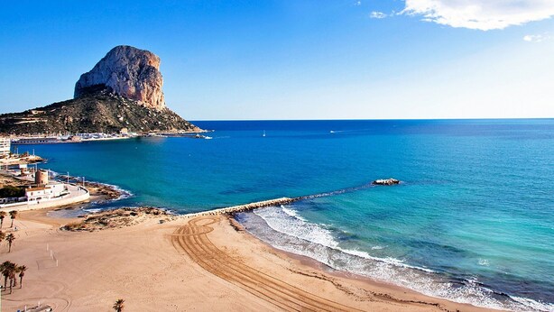 A coastal landscape with a prominent rock formation, a sandy beach, and a pier extending into the sea. - Cosy apartment for 2 people with A/C, WIFI, pool, TV and terrace (Calpe)