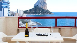 A balcony with a table set for two, overlooking a coastal view with a prominent rock formation and a cityscape in the background. - Cosy apartment for 2 people with A/C, WIFI, pool, TV and terrace (Calpe)