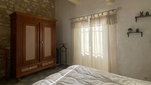 Un dormitorio con cama, armario de madera, pared de piedra y ventana con cortinas.