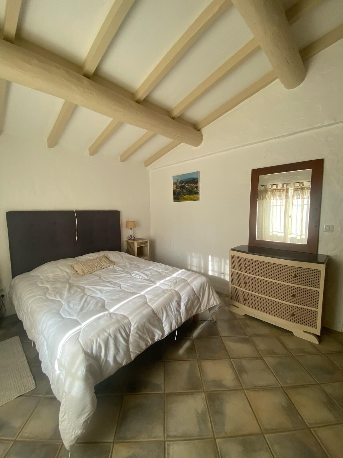Quarto com cama, penteadeira, mesa de cabeceira, luminária e quadro na parede.