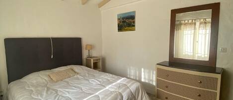 Quarto com cama, penteadeira, mesa de cabeceira, luminária e quadro na parede.