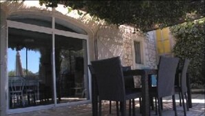 Un patio exterior con una mesa, sillas, un vidrio que da a un jardín y un muro de piedra.