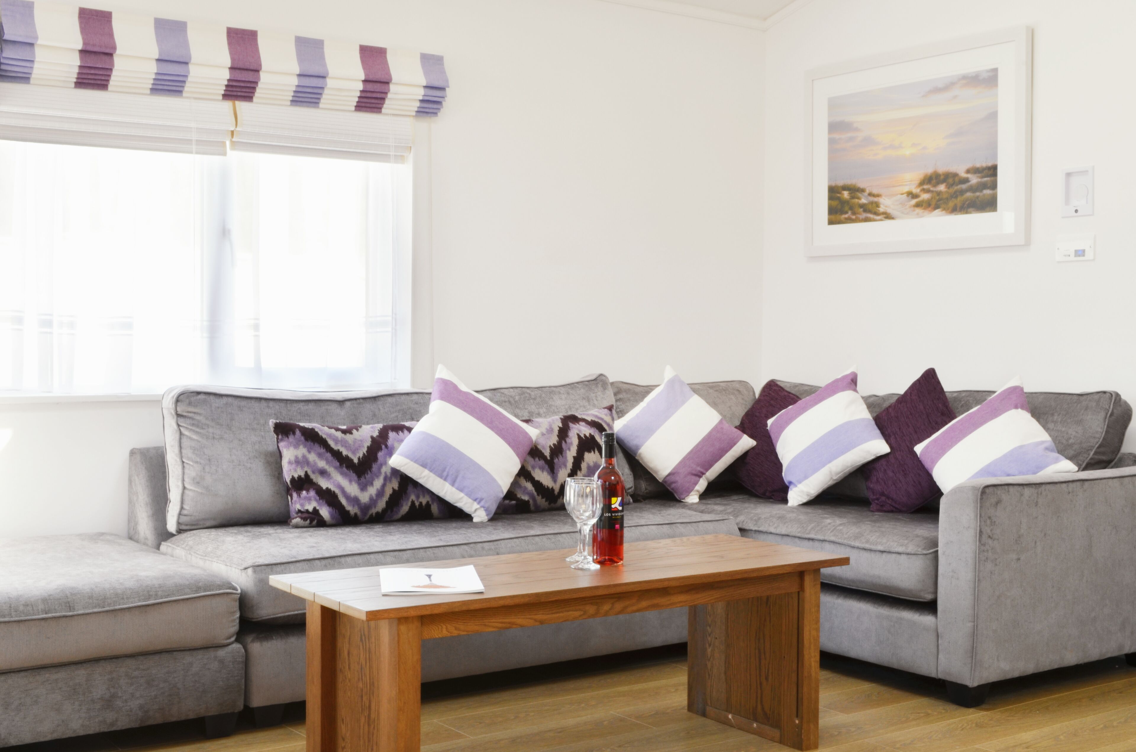 Una sala de estar moderna con un sofá gris, cojines a rayas, una mesa de centro de madera y un cuadro con paisaje en la pared.