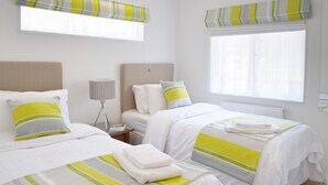 A hotel room with two beds, a bedside table, a lamp, and a window with curtains. - Luxury Lodge, South Devon Coast nr Plymouth, 200m to Beach + Indoor Heated Pool, (Nr Plymouth)