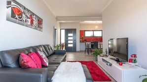 Ein modernes Wohnzimmer mit einem schwarzen Ledersofa, einem weißen, flauschigen Teppich und einem roten Teppich. Ein Flachbildfernseher steht auf einem weißen Konsolentisch.