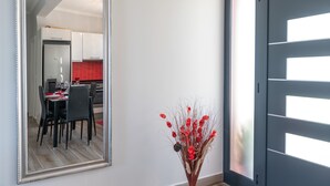 Eine moderne Küche mit weißen Schränken und einer roten Spritzschutzwand, ein Essbereich mit Tisch und Stühlen sowie eine dekorative Vase mit roten Blumen.