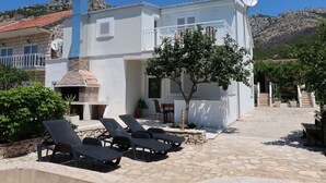 A two-story building with a stone facade, a chimney, and a satellite dish. There are lounge chairs and a small pool area in front.