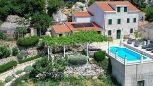 A villa with a swimming pool, stone walls, and a garden with various plants and a pergola.