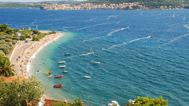 A coastal town with a beach, boats, and a distant cityscape.