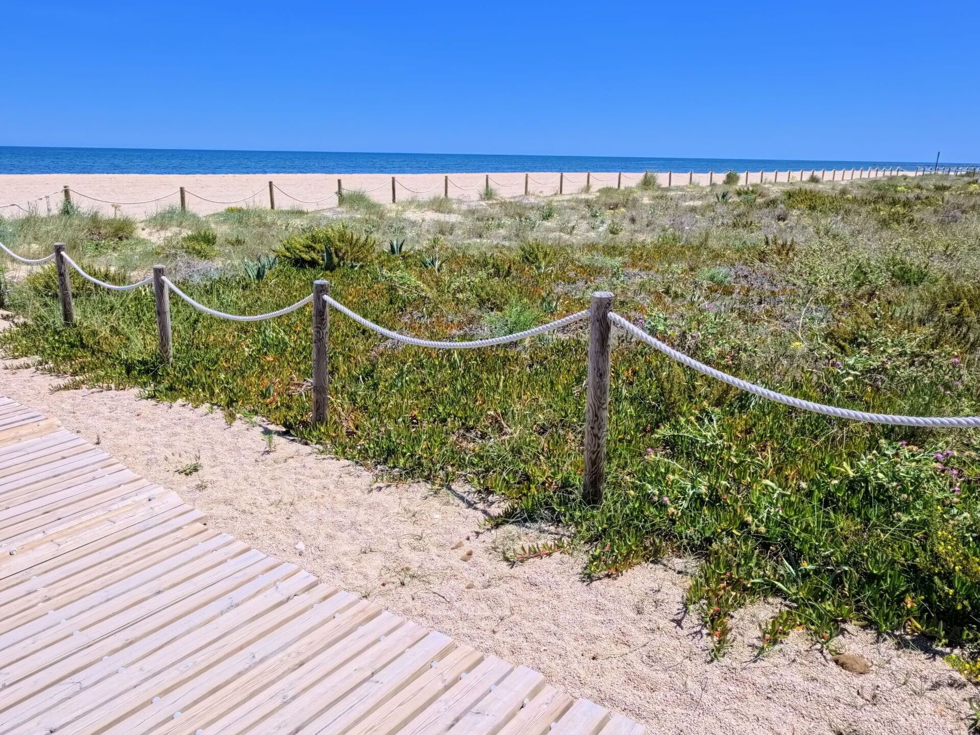 Une promenade en bois menant à une plage, avec une barrière faite de cordes.