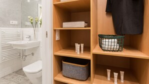 A bathroom with a white sink, a mirror, and a toilet. There are wooden shelves with storage boxes and a green basket.