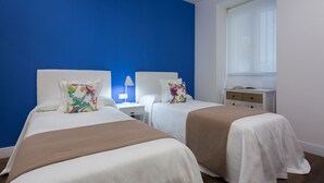 A hotel room with two beds, a nightstand with a lamp, a window with a view, and a dresser.