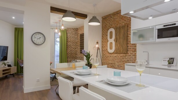 A modern kitchen with white countertops, a large island, and a brick accent wall.