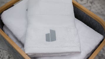 Una cesta de madera llena de toallas blancas dobladas, sobre un piso con diseño.