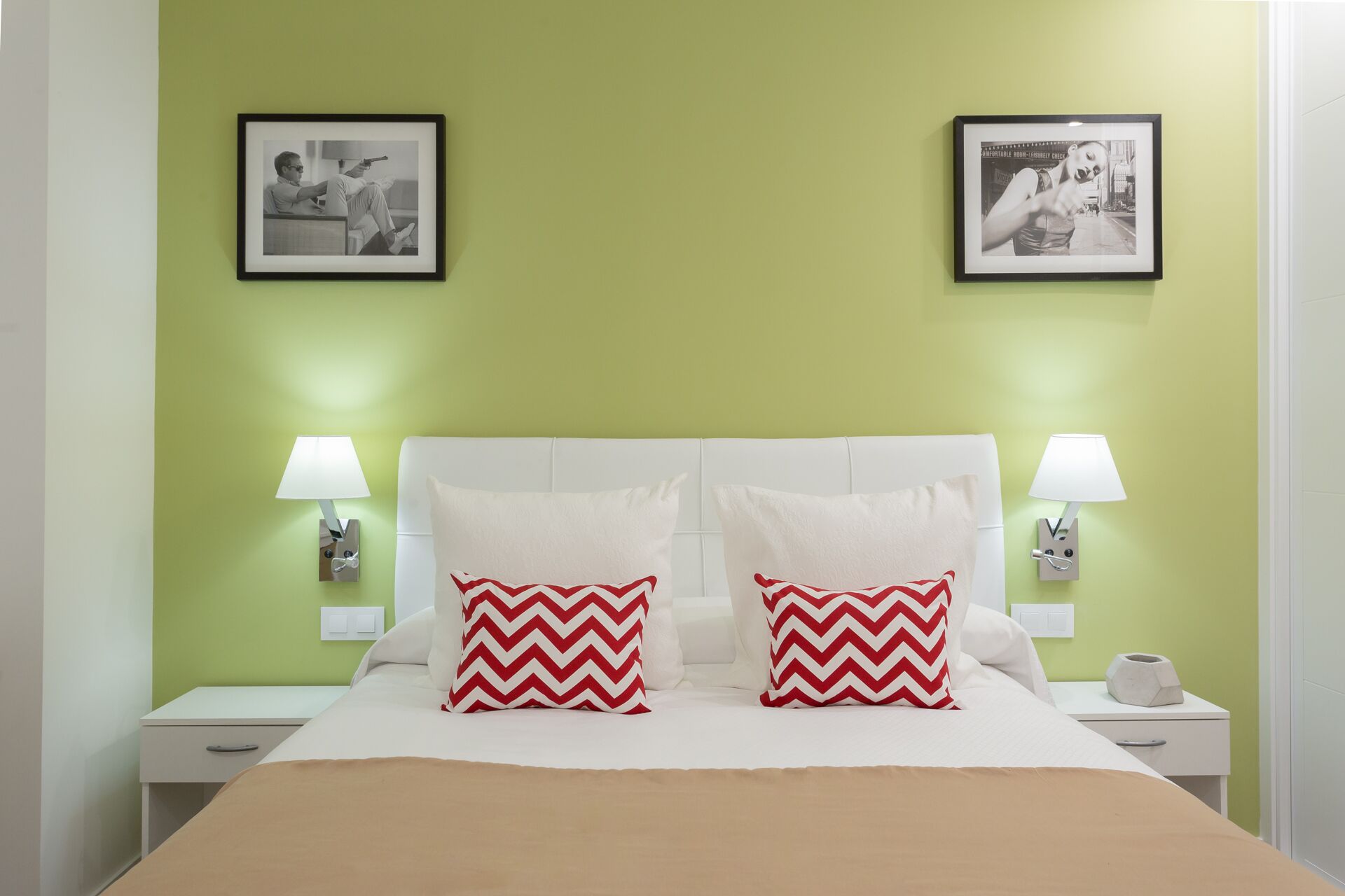 A hotel room with a green wall, two framed pictures, white bedding, and two nightstands with lamps.